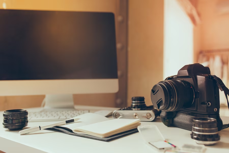 Desk with camera, computer, and notebook