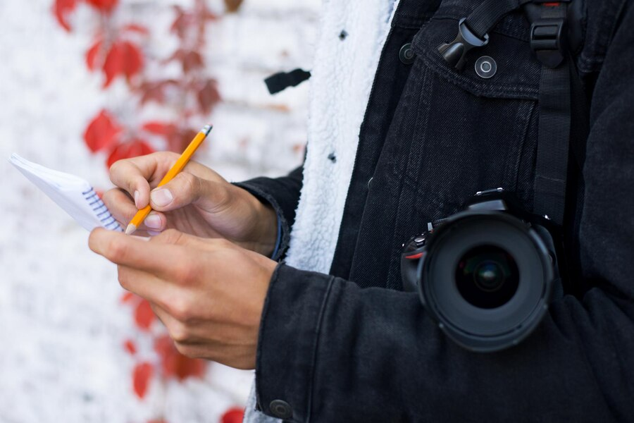 Person writing on a notebook and carrying a camera